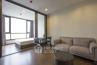 Modern open-plan living room with cozy sofa and dining area, adjacent to a bright bedroom with large windows.