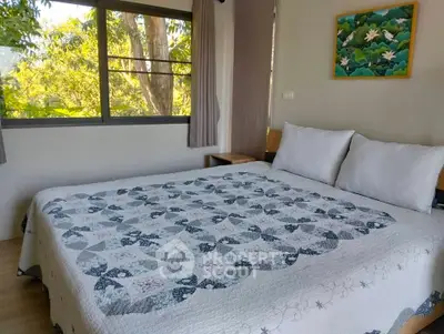 Cozy bedroom with large window and nature view, featuring a stylish quilted bedspread.