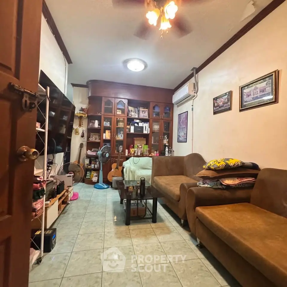 Cozy living room with brown sofas, wooden shelves, and a ceiling fan, perfect for relaxation and entertainment.