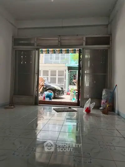 Spacious tiled room with large sliding doors opening to a street view, ideal for versatile use.