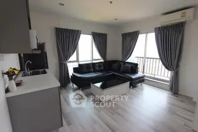 Modern living room with sleek black sofa and large windows offering natural light.
