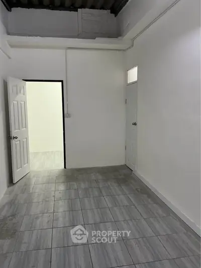 Spacious empty room with tiled flooring and two doors, ideal for customization.