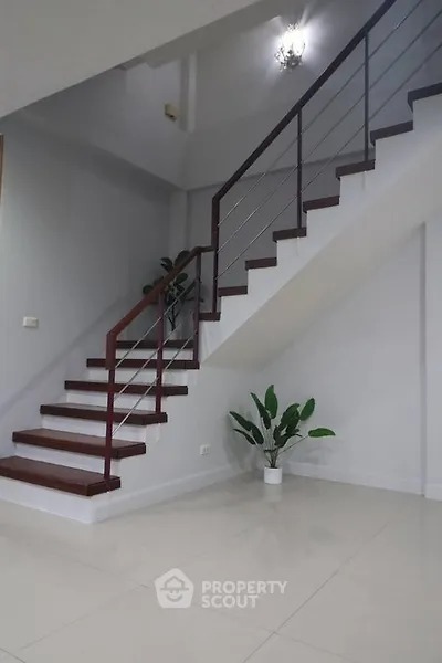 Elegant staircase with modern railing and potted plants in a minimalist home interior.