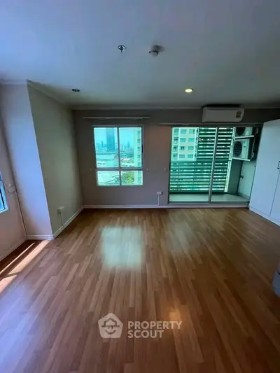 Spacious living room with wooden flooring and large windows offering city views.