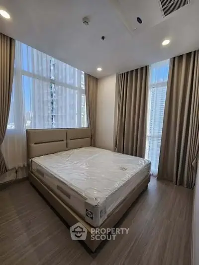 Spacious bedroom with large windows and modern decor in a high-rise apartment.