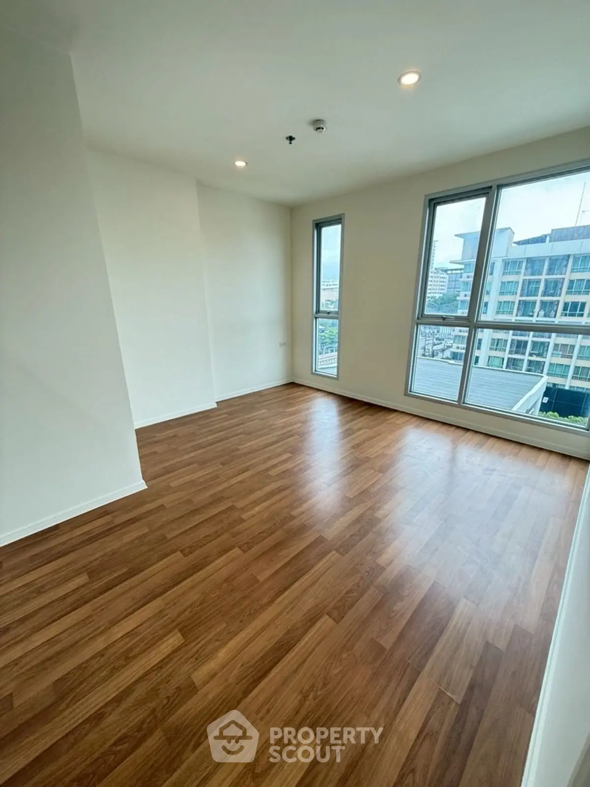 Spacious empty room with large windows and wooden flooring, offering city views.