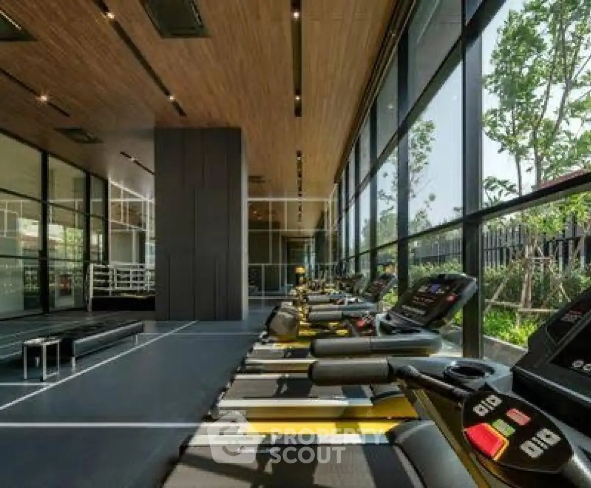 Modern gym with treadmills and large windows offering garden views.