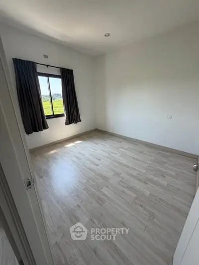 Spacious empty bedroom with wooden flooring and large window view.