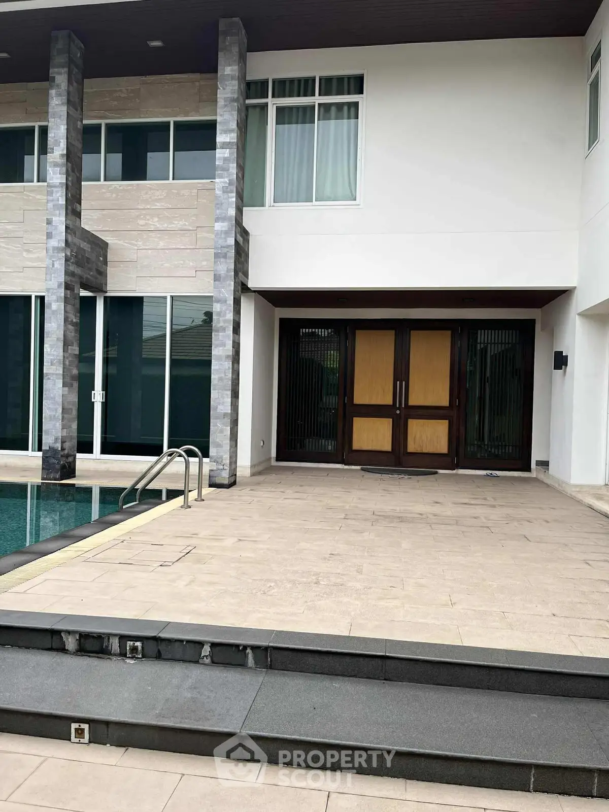 Luxurious modern home exterior with poolside patio and elegant entrance.