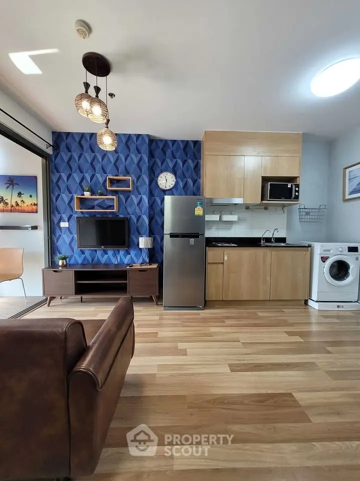 Modern living room with open kitchen, featuring stylish decor and appliances like fridge and washing machine.