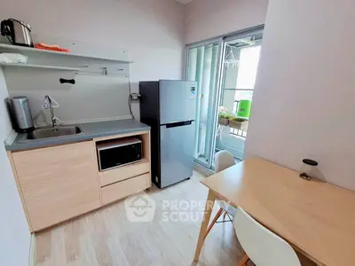 Modern compact kitchen with fridge, microwave, and dining area in bright apartment.