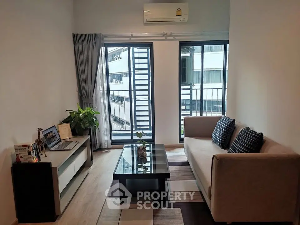 Modern living room with sofa, coffee table, and large windows offering natural light.