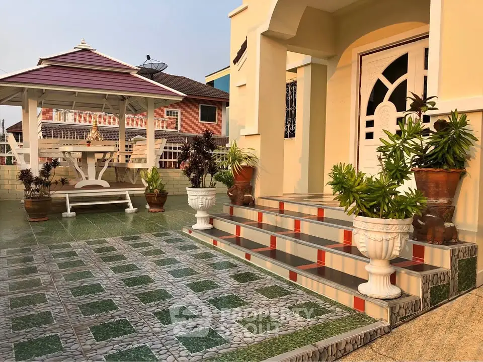 Charming home entrance with elegant steps and lush greenery, featuring a stylish gazebo in a serene setting.