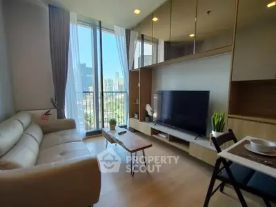 Modern living room with large TV and city view from balcony, featuring sleek furniture and natural light.