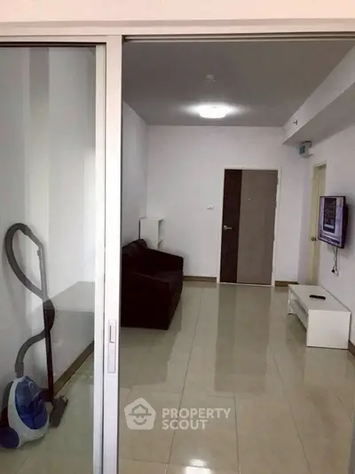 Modern living room with sleek tile flooring and minimalist decor, featuring a wall-mounted TV and a vacuum cleaner.