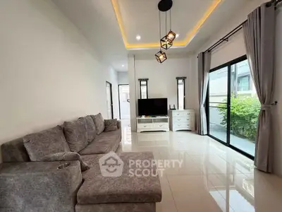 Modern living room with stylish lighting and large windows, featuring a cozy gray sectional sofa.