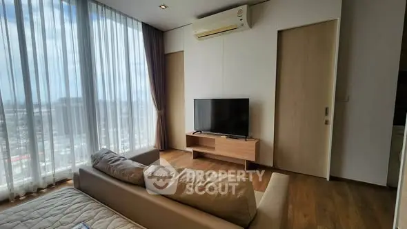 Modern living room with large windows and city view, featuring a sleek TV setup and cozy sofa.
