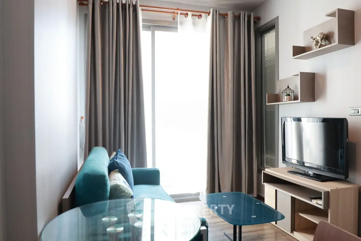 Modern living room with teal sofa, glass coffee table, and wall-mounted TV unit.