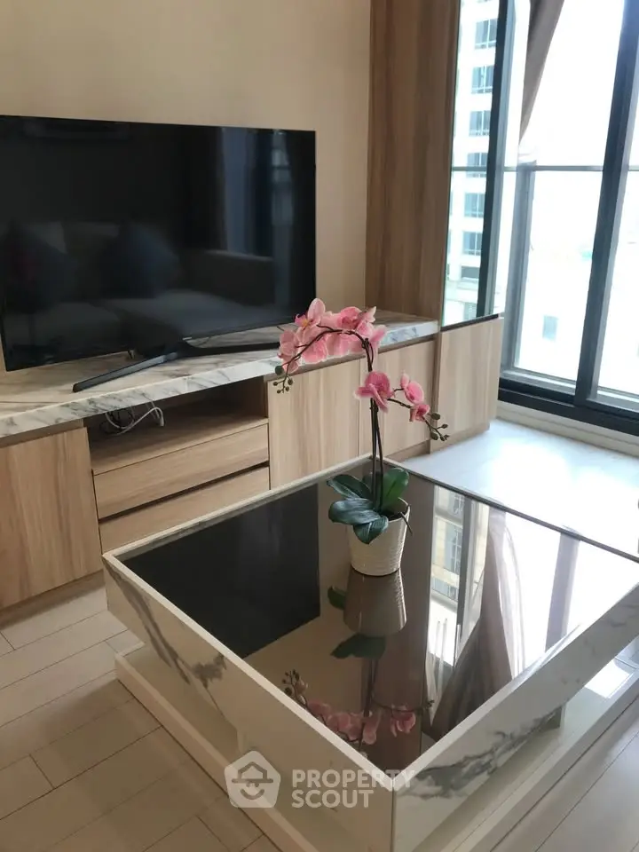 Modern living room with stylish furniture and large TV, featuring a glass coffee table and elegant decor.