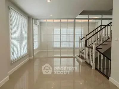 Spacious modern living room with elegant staircase and large windows for natural light.