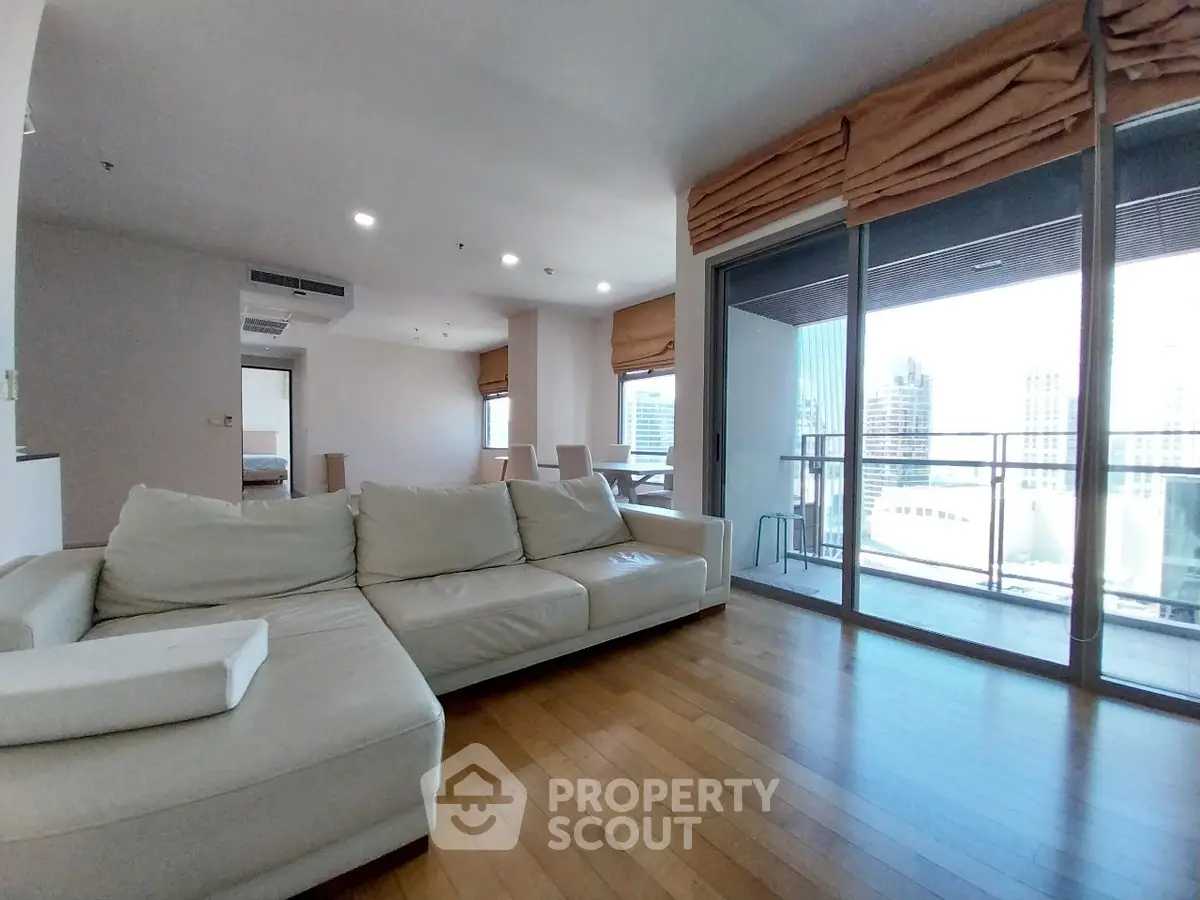 Spacious modern living room with large balcony and city view, featuring elegant wooden flooring and cozy seating.