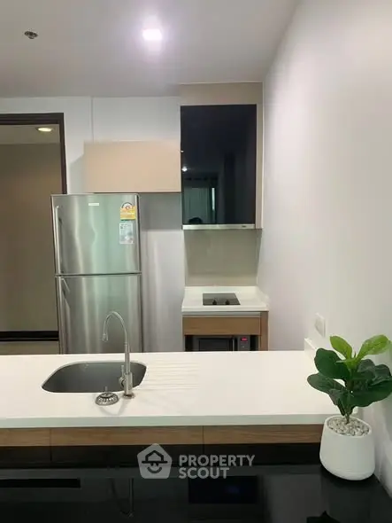 Modern kitchen with sleek design, featuring stainless steel fridge and built-in cooktop.