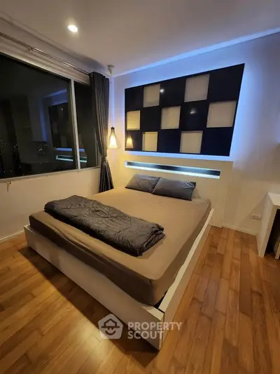 Modern bedroom with stylish decor and large window offering city views, featuring a cozy bed and ambient lighting.
