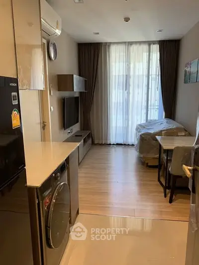 Modern living room with open kitchen and washing machine, featuring elegant decor and natural light.
