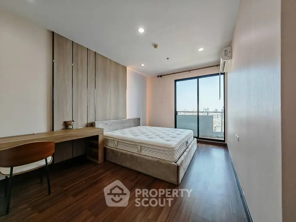 Spacious bedroom with city view and modern furnishings in high-rise apartment.