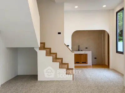 Modern minimalist interior with staircase and open kitchen layout, featuring sleek design and natural light.