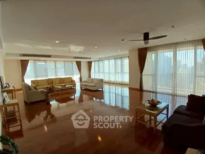 Spacious living room with large windows and city view, featuring elegant furniture and polished wooden floors.