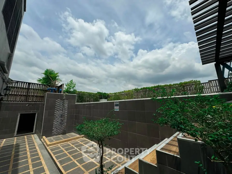 Modern outdoor terrace with stylish tiles and lush greenery under a bright blue sky.