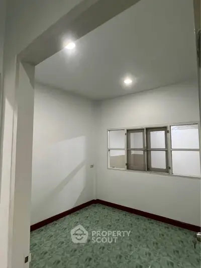 Spacious room with green flooring and white walls, featuring a window for natural light.