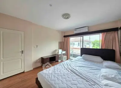 Spacious bedroom with large window and modern furnishings in a well-lit apartment.