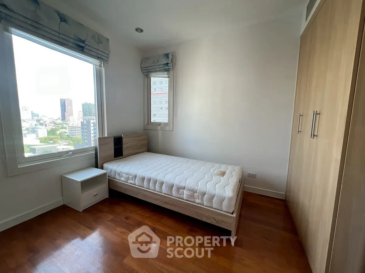 Bright bedroom with single bed and city view, featuring wooden flooring and built-in wardrobe.