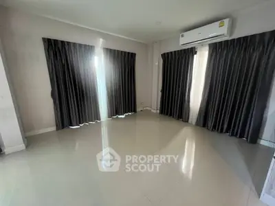Spacious empty room with glossy tiled floor and large windows with curtains.