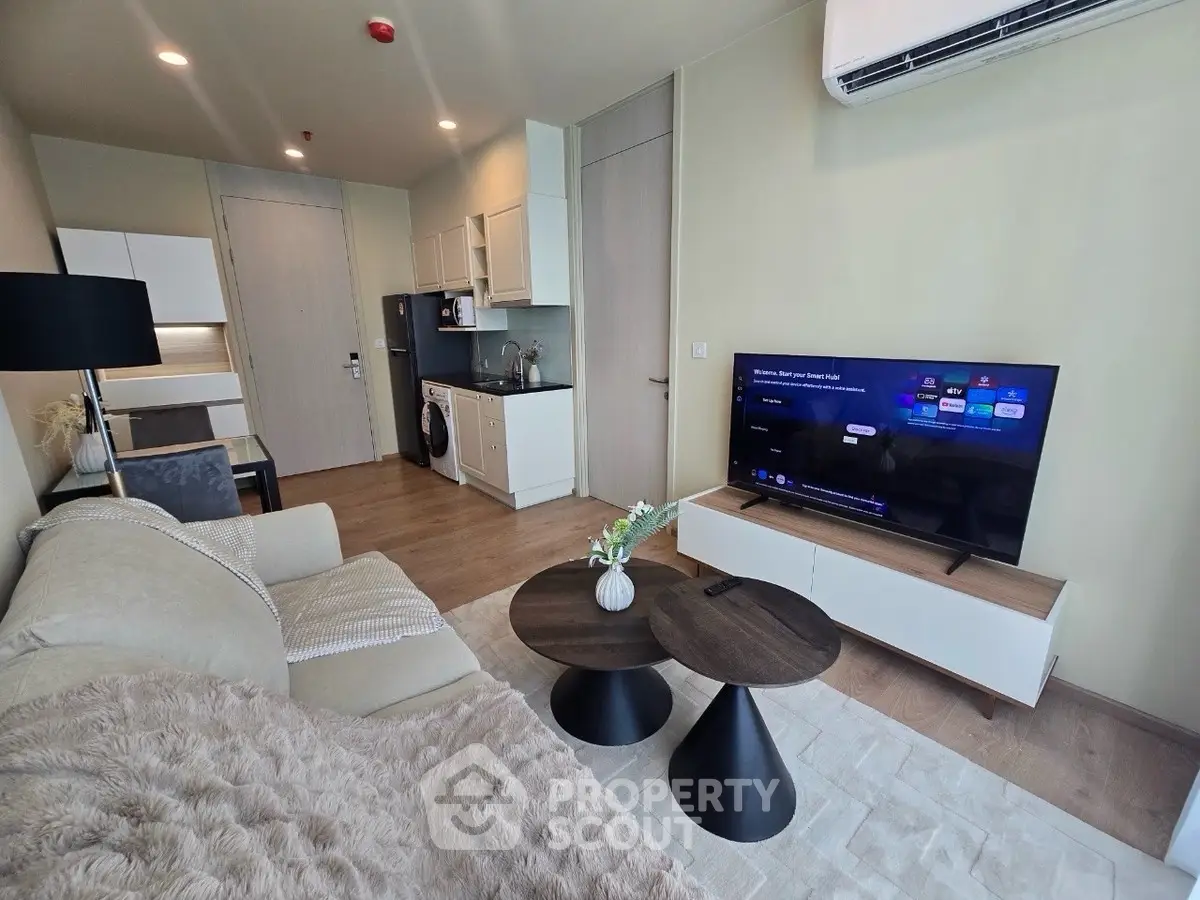 Modern living room with cozy sofa, TV, and compact kitchen area in open layout apartment.