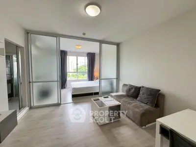 Modern living room with frosted glass partition leading to a bright bedroom, featuring sleek furniture and natural light.