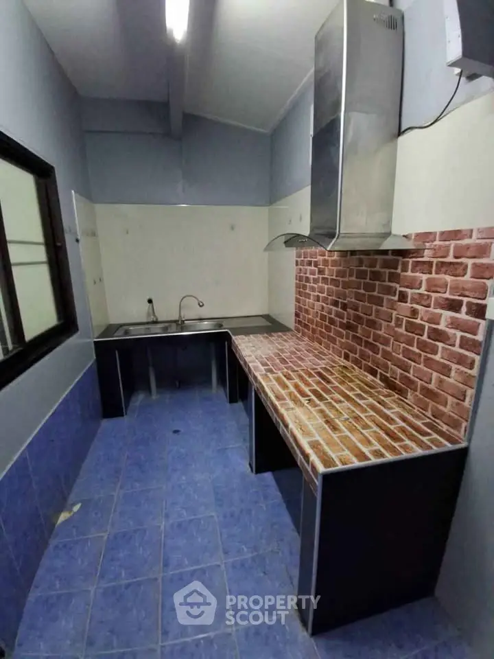 Modern kitchen with brick backsplash and blue tile flooring, featuring stainless steel sink and range hood.