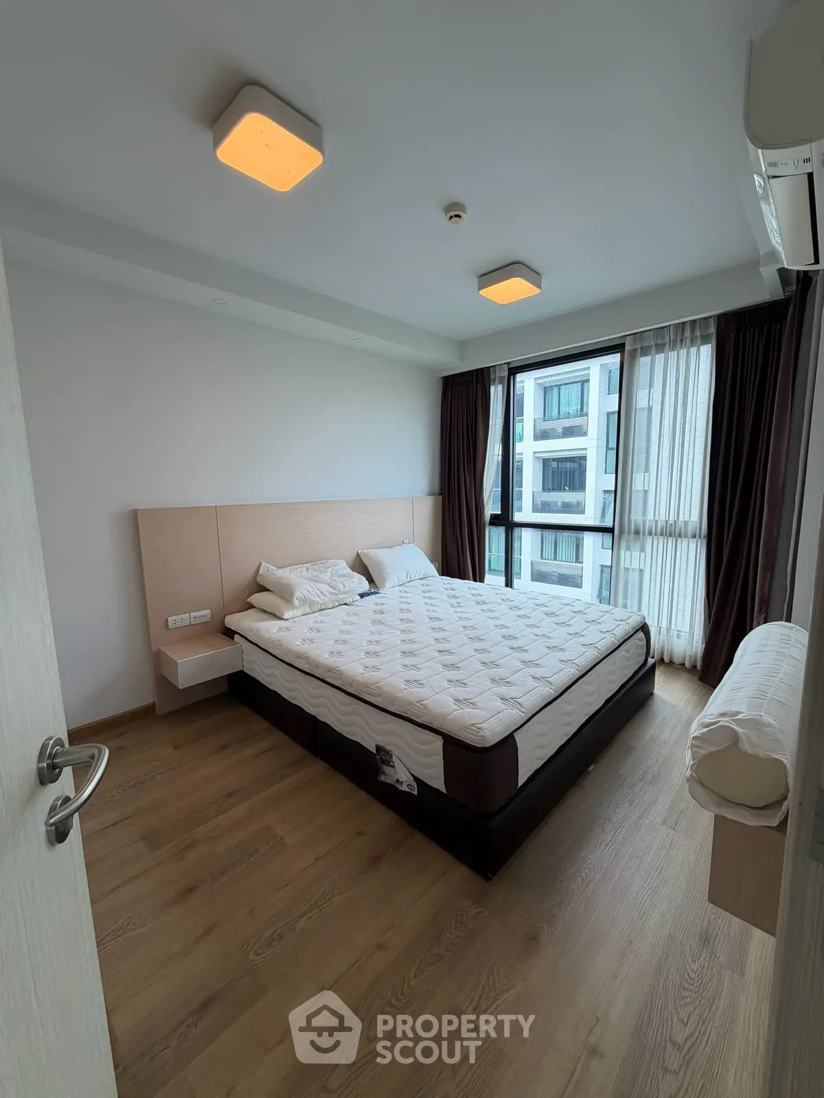 Modern bedroom with large window and wooden flooring in a stylish apartment.