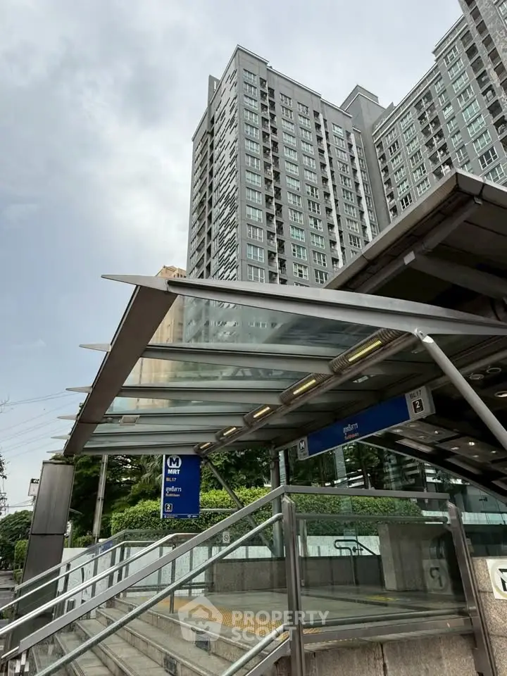 Modern high-rise building near metro entrance with glass canopy, showcasing urban convenience and accessibility.