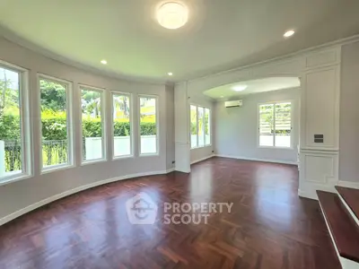 Spacious living room with elegant hardwood floors and large windows offering lush garden views.