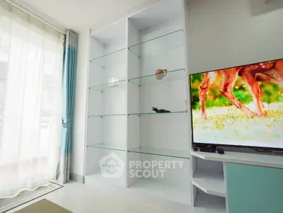 Modern living room with glass shelves and large TV, featuring elegant decor and natural light.