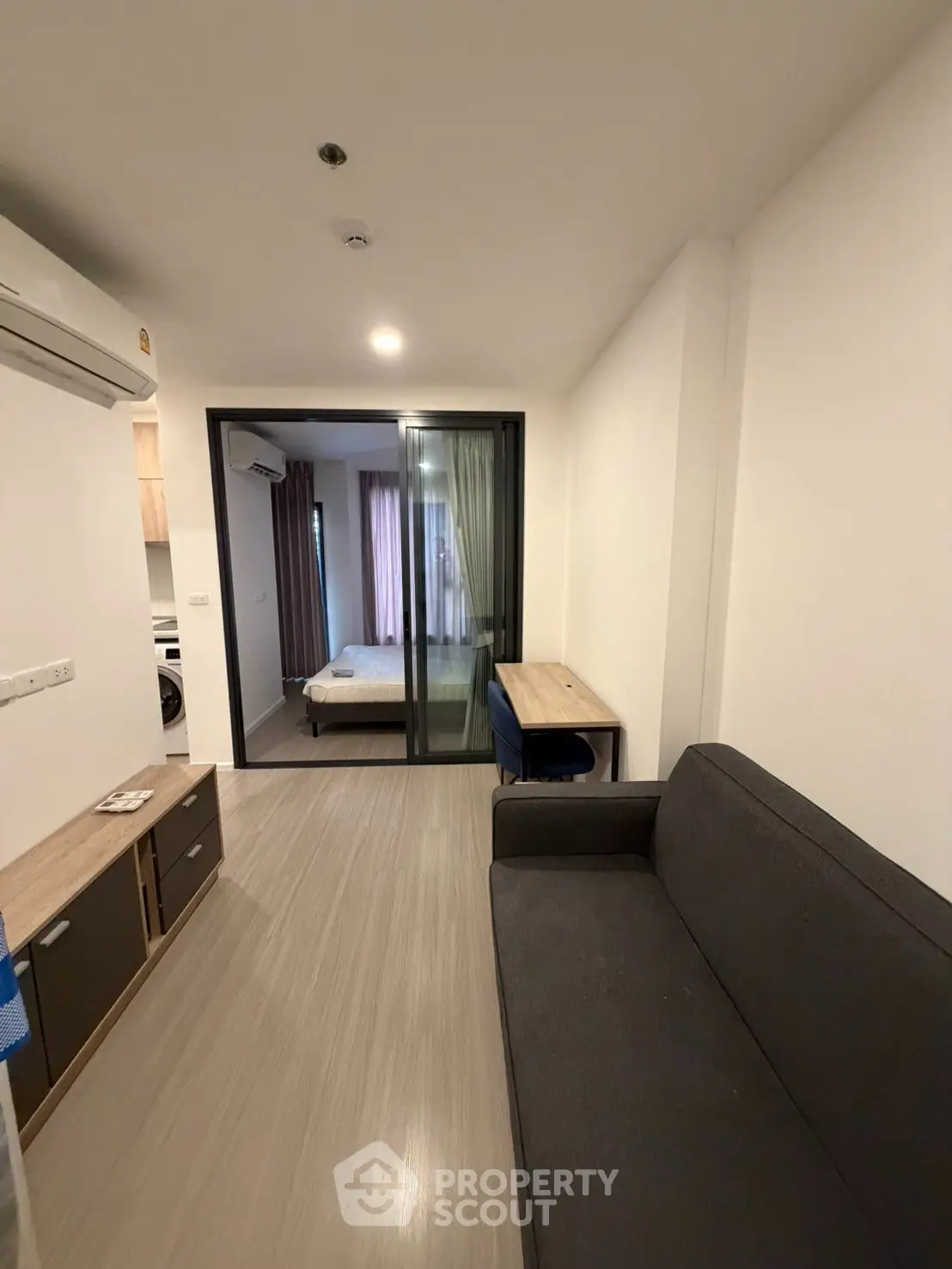 Modern apartment interior with cozy living room and bedroom separated by glass doors, featuring sleek furniture.