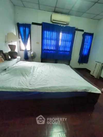 Cozy bedroom with blue curtains and air conditioning, featuring a comfortable bed and wooden flooring.
