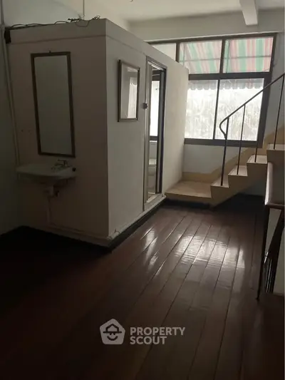 Unique interior space with wooden flooring and staircase, featuring a compact enclosed area with a sink.