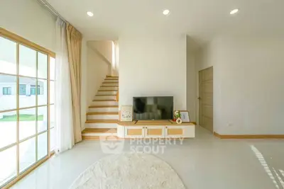 Bright modern living room with TV, staircase, and large window for natural light.