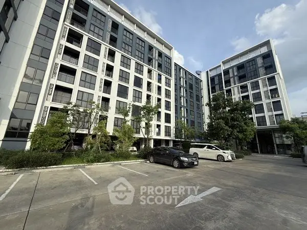 Modern apartment building with spacious parking area and lush greenery.
