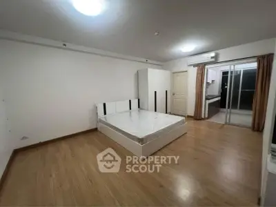 Spacious bedroom with wooden flooring and modern furniture in a well-lit apartment.