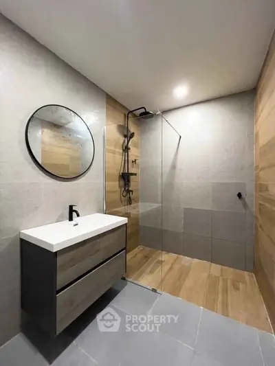 Modern bathroom with sleek design, featuring a round mirror and glass shower enclosure.